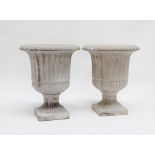A pair of campana style urns - reconstituted stone, of fluted form and raised on a square base,