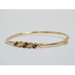 A diamond and sapphire bangle - the crossover setting in 14ct yellow gold, weight 5g.