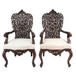 A pair of Anglo-Indian hardwood armchairs, ornately carved and varnished with perforated foliate