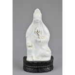 A Chinese Blanc de Chine porcelain figure of Guanyin on a separate carved wooden base. 19.5cm tall