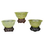 THREE CHINESE 'SPINACH JADE' BOWLS ON STANDS, 20TH CENTURY. Each bowl with rounded body on a shallow