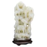 A CHINESE PALE CELADON JADE CARVING ON WOODEN STAND. Carved and pierced in the form of a rock