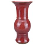 A CHINESE SANG-DE-BOEUF PORCELAIN GU-FORM BEAKER VASE. Covered in a dark red speckled glaze thinning