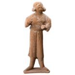 A CHINESE RED POTTERY MODEL OF A GROOM, TANG DYNASTY (618-907). The figure standing with arms raised