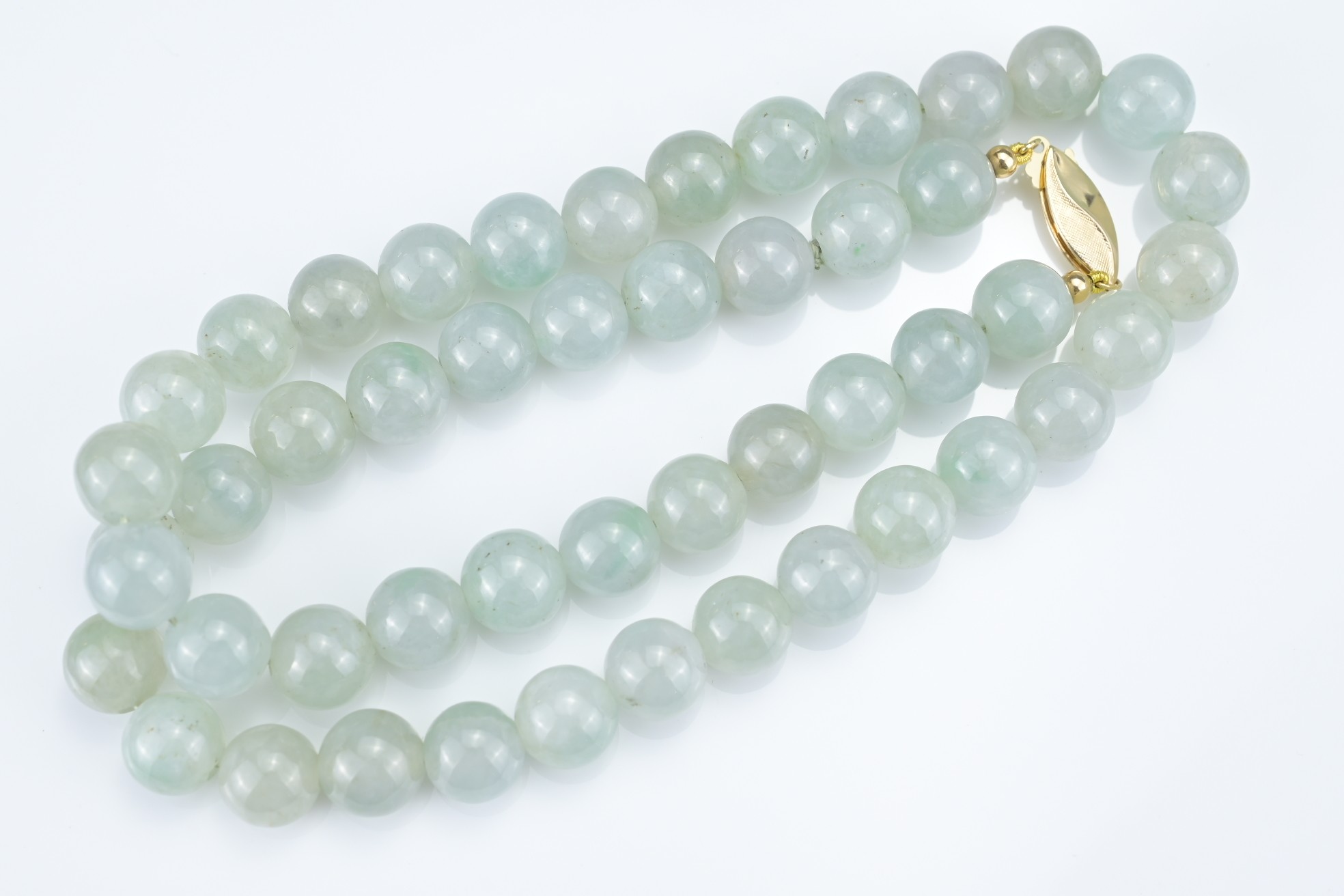 A PALE GREEN JADEITE SINGLE STRAND BEADED NECKLACE WITH 18KT YELLOW GOLD CLASP. The marquise-