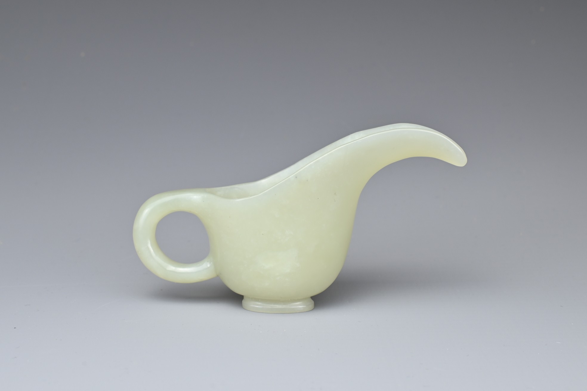 A CHINESE PALE CELADON JADE CUP. Of slender form with a looped handle and curved spout. 10.5cm