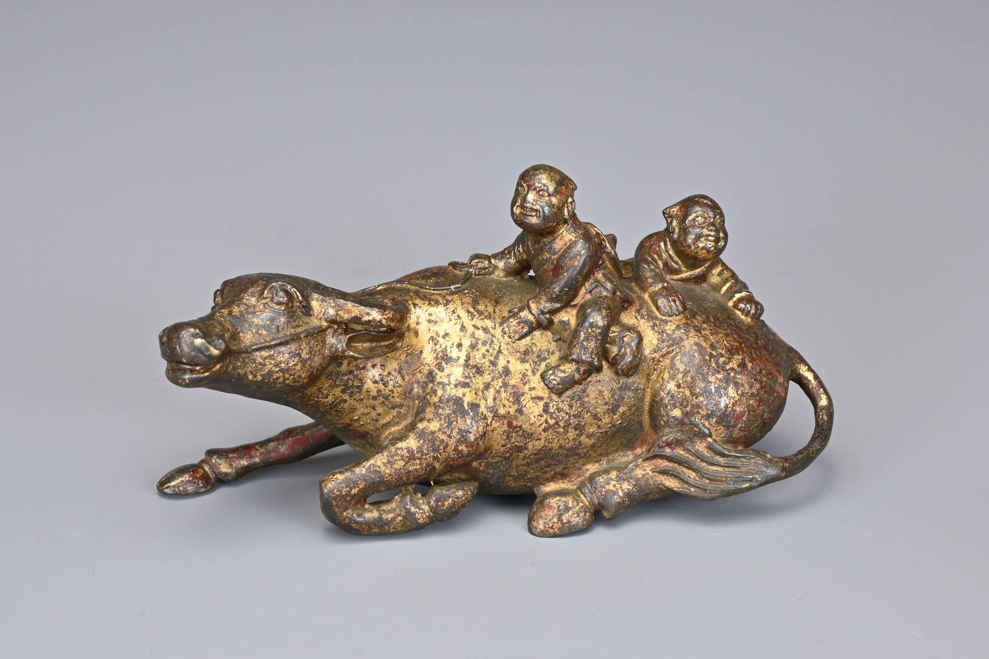 A CHINESE GILT BRONZE MODEL OF A BUFFALO AND BOYS. The recumbent buffalo wearing a rein with on