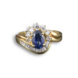 AN 18KT YELLOW GOLD, SAPPHIRE AND DIAMOND CLUSTER RING. The central sapphire flanked by diamonds,