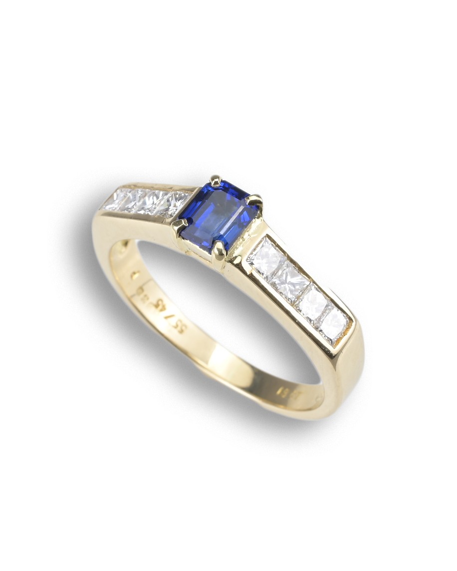 AN 18CT DIAMOND AND SAPPHIRE DRESS RING. Emerald cut 0.63ct sapphire set in 18ct yellow gold with