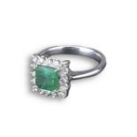 AN 18KT WHITE GOLD EMERALD AND DIAMOND CLUSTER RING. With central square step cut emerald flanked by