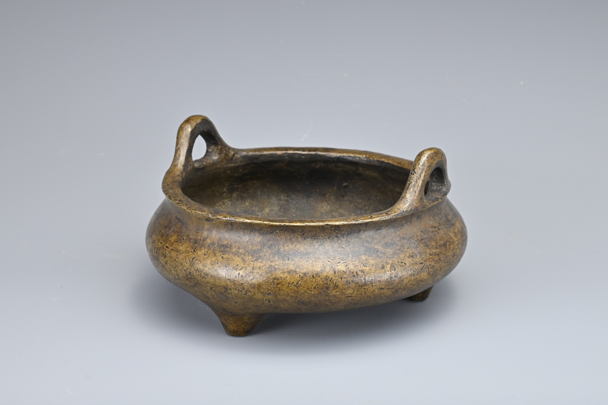 A CHINESE BRONZE TRIPOD CENSER. Of squat circular form with two looped handles on three conical