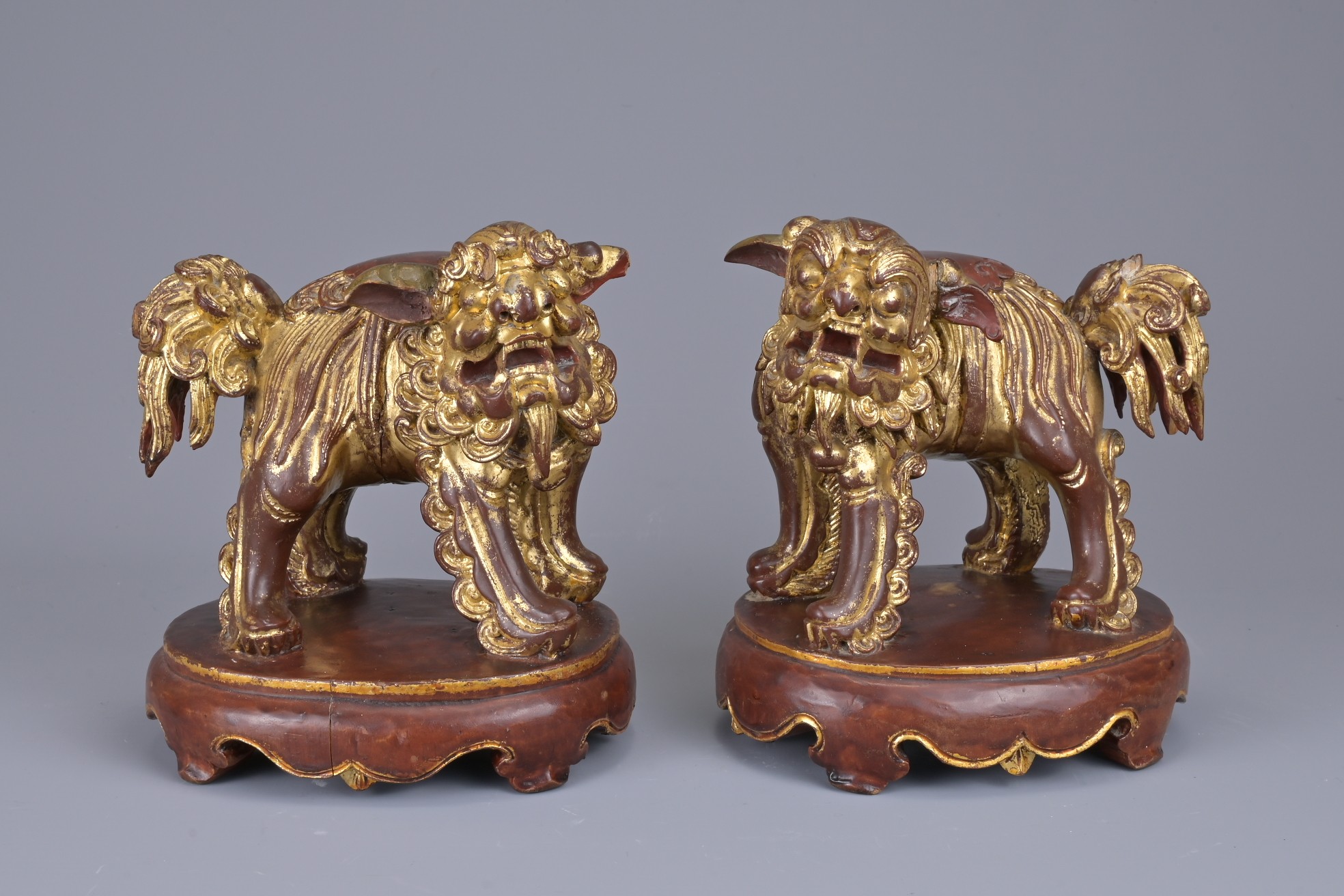 A PAIR OF CHINESE CARVED WOOD GILT LACQUERED LIONS. Standing fiercely with bushy tail. Ruyi head