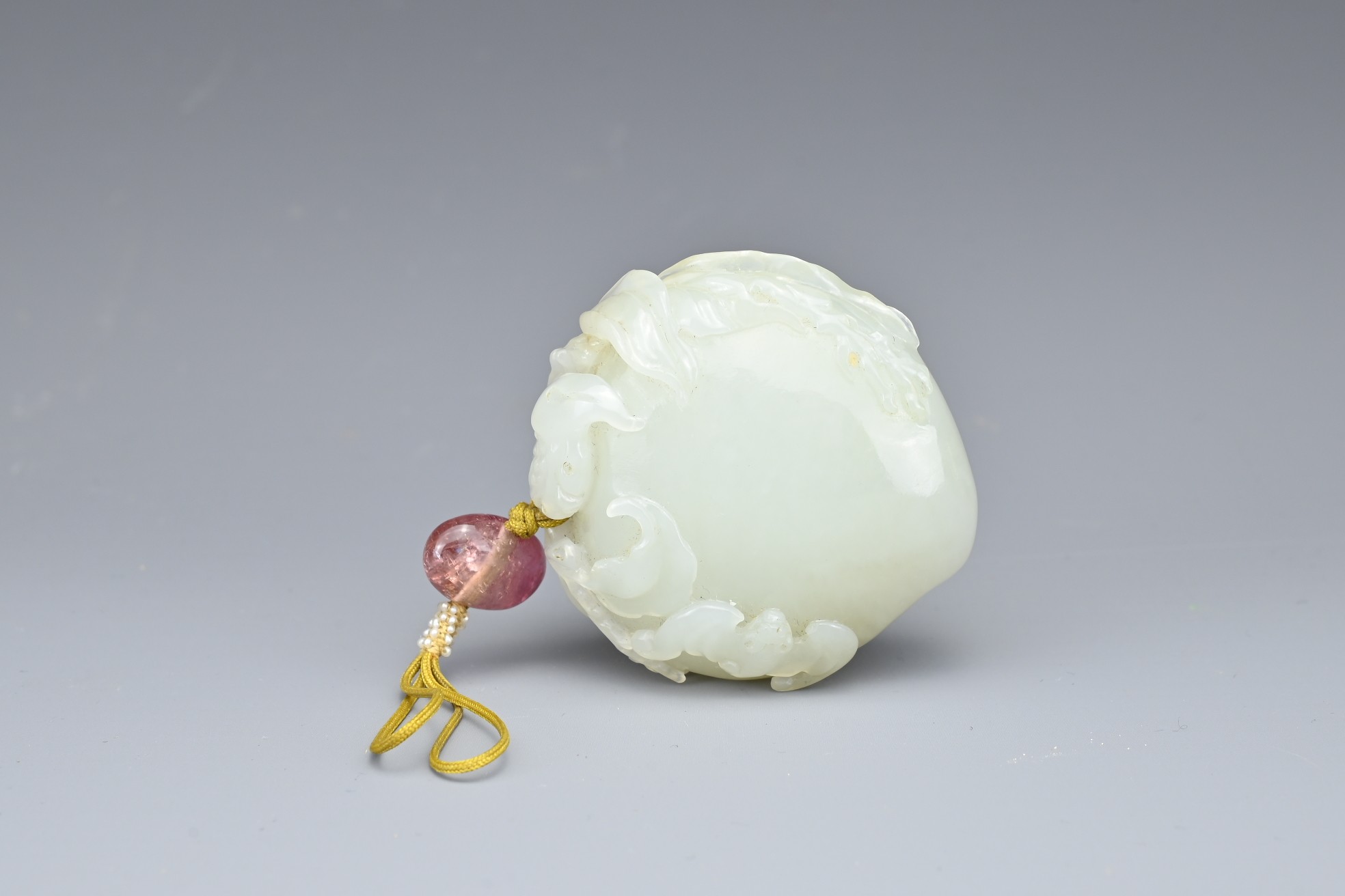 A CHINESE PALE CELADON JADE PEACH AND BAT GROUP, QING DYNASTY. The peach carved in relief with a