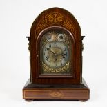 An English table clock in veneered wood, decorated with inlaid motifs. Early twentieth century.