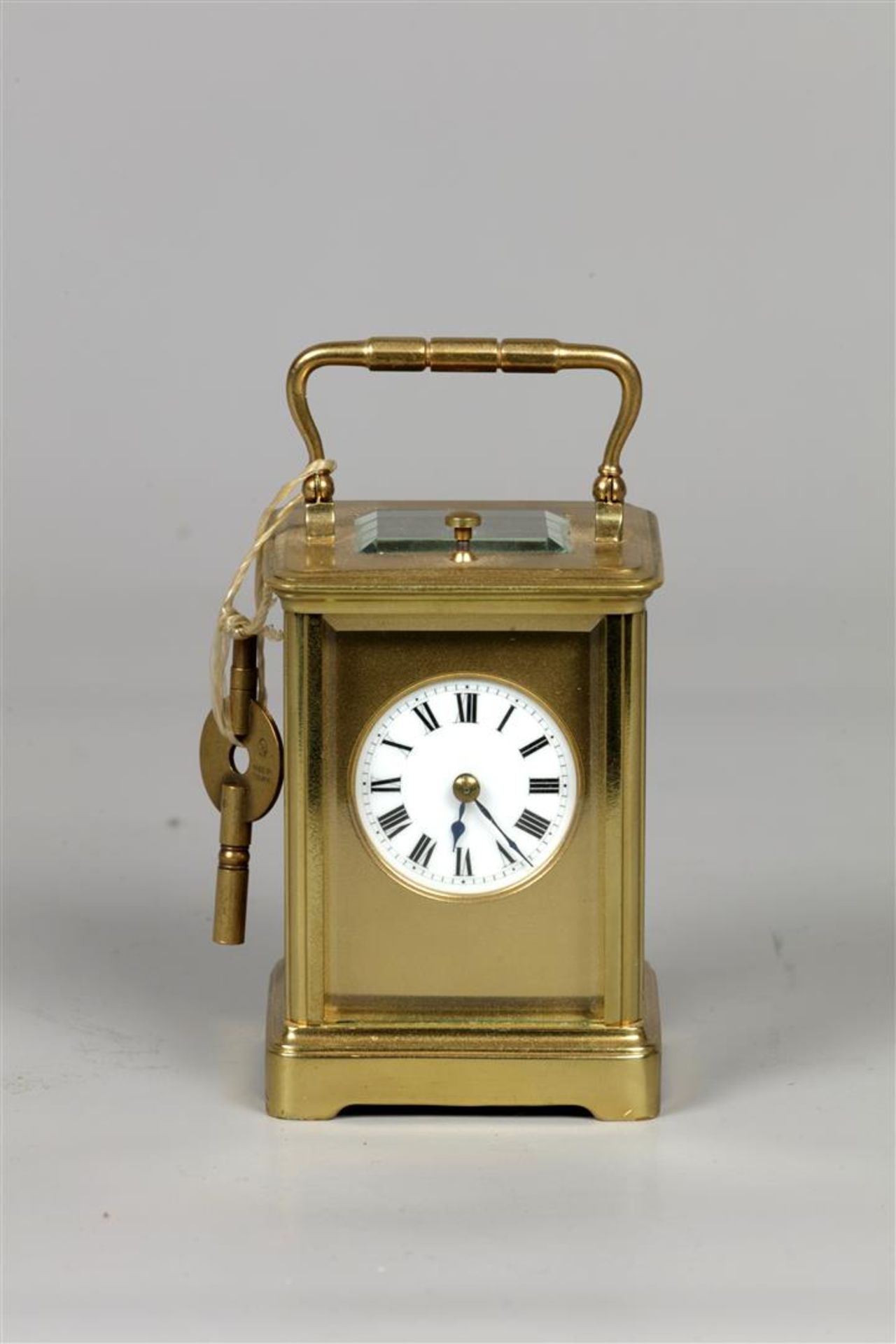 A brass travel alarm clock, white enamel dial shows the hou