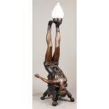A bronze lamp holder in the shape of an acrobat, resting on