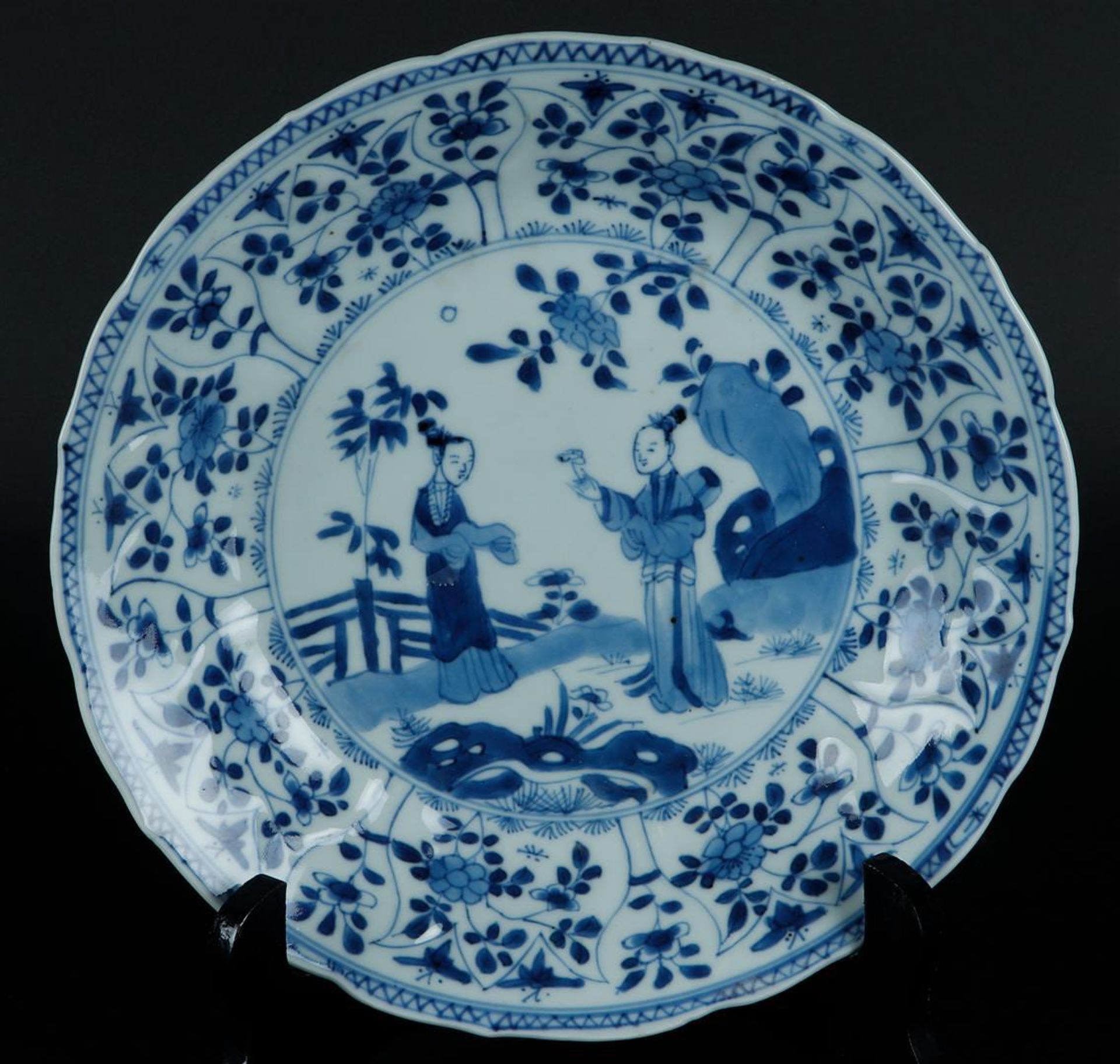 A porcelain plate with a tulip outer rim with floral decor and butterflies. The center with two long