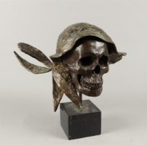 A brown patinated bronze sculpture in the shape of a skull, on a marble base.