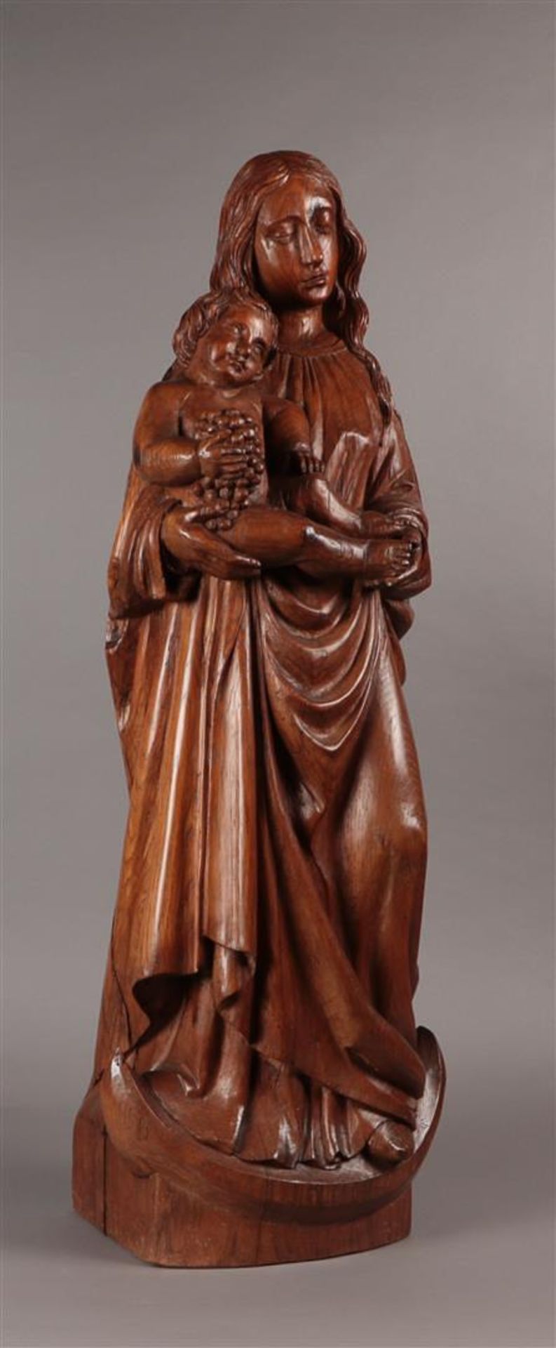 An oak statue depicting Madonna standing on the moon disk, carying the Child Jesus with a bunch of g