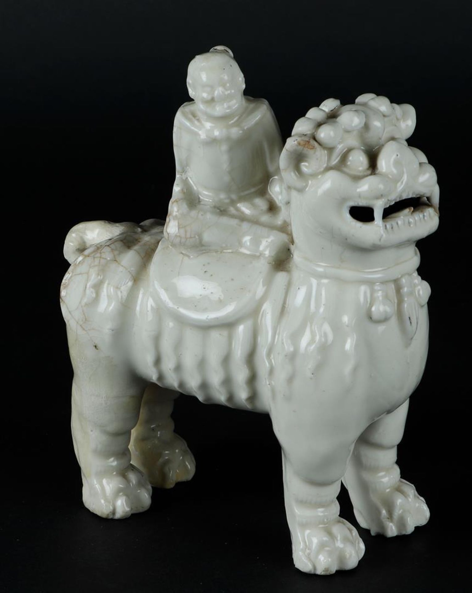 A porcelain blanc de chine foo dog with a figure on it. China, Kangxi.
