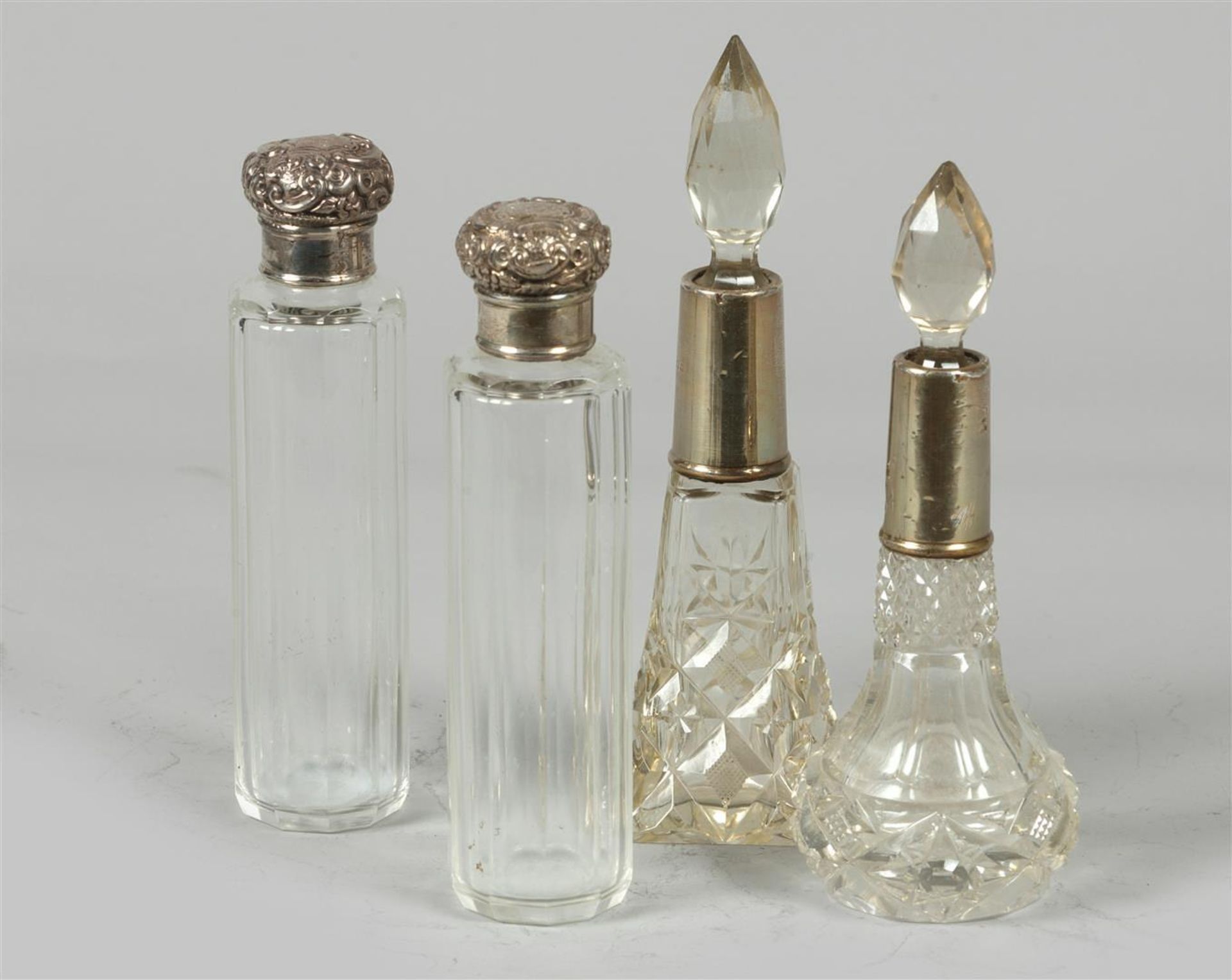 A lot consisting of (4) lotion bottles of cut glass with silver mounts or stoppers.