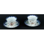 Two porcelain cups and saucers, contoured with floral blue decor, between which are golden flowers a