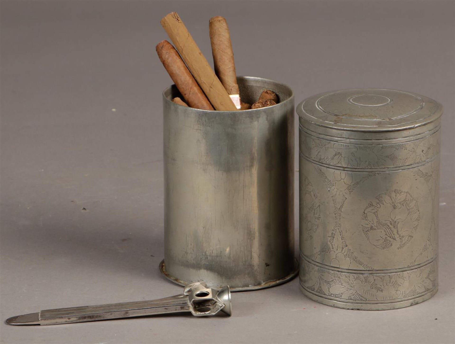 A tin cigar box, Indonesia, with cigars and silver (3rd grade) cigar cutter.