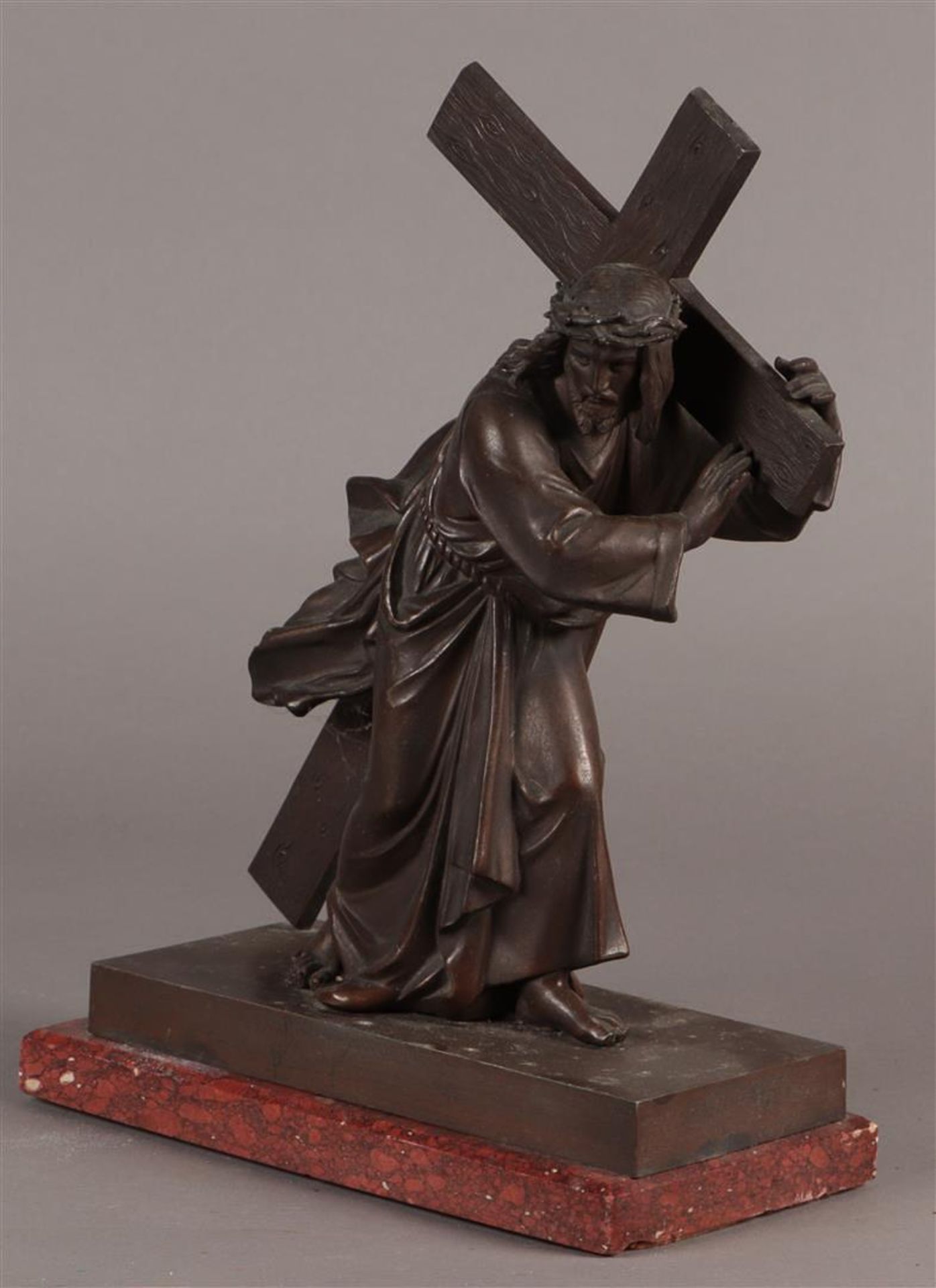 A bronze sculpture of Christ carrying the cross. Mounted on a red marble base.