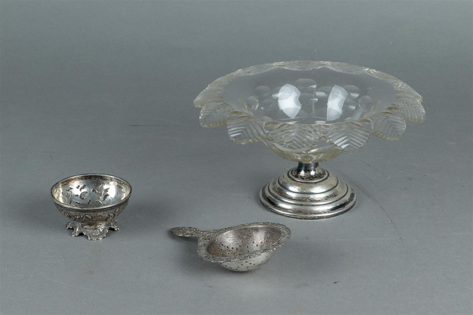 A bonbon dish made of pressed glass on a silver base. And a tea strainer.