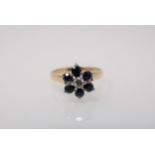 A Diamond and Sapphire Cluster Ring claw-set brilliant-cut diamond within frame of six round