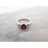 A Ruby and Diamond three stone Ring claw-set round ruby, 1ct, between two brilliant-cut diamonds in