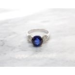 A Sapphire and Diamond three stone Ring claw-set round fine sapphire, 2.65cts, between two brilliant