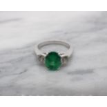 An Emerald and Diamond three stone Ring claw-set oval-cut emerald between two brilliant-cut diamonds