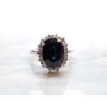 A Sapphire and Diamond Cluster Ring claw-set oval-cut sapphire, 3.04cts, within a frame of