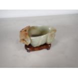 An Oriental jade lotus blossom Bowl with carved leafage design on a hardwood stand, 4 in long