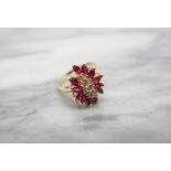 A Diamond and Ruby Cluster Ring claw-set a row of five brilliant-cut diamonds within a frame of