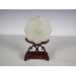 A Chinese celadon Jade Bi Disk carved flower head with geometric carved centre section on hardwood
