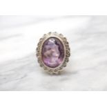An Amethyst and Diamond Cluster Ring rubover-set oval-cut amethyst within a frame of illusion-set