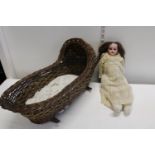 A Victorian bisque headed doll in a antique wicker crib