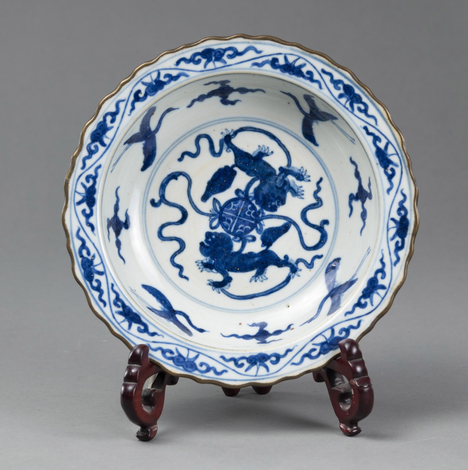 A BLUE AND WHITE FOLDED EDGE DISH DECORATED WITH LIONS, CRANES AND HORSES, WITH A WOODEN STAND