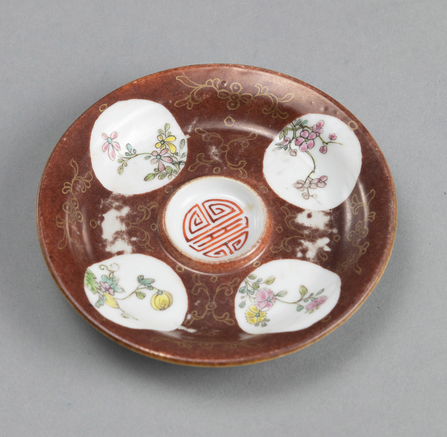 A SMALL REDDISH-BROWN GLAZED SAUCER WITH A 'SHOU' CHARACTER AND FOUR FLORAL MEDALLIONS IN POLYCHROM