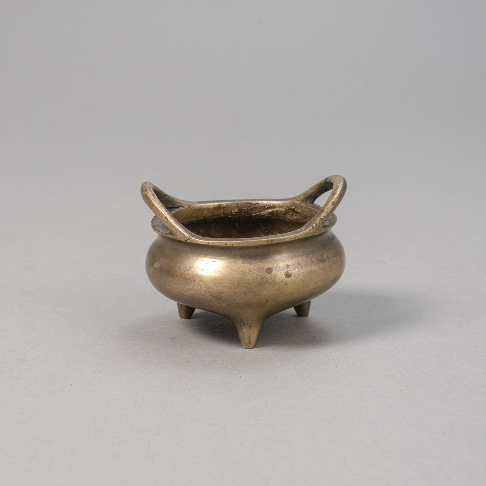 A SMALL BRONZE INCENSE BURNER ON THREE SHORT FEET, INSIDE DRAGON RELIEF