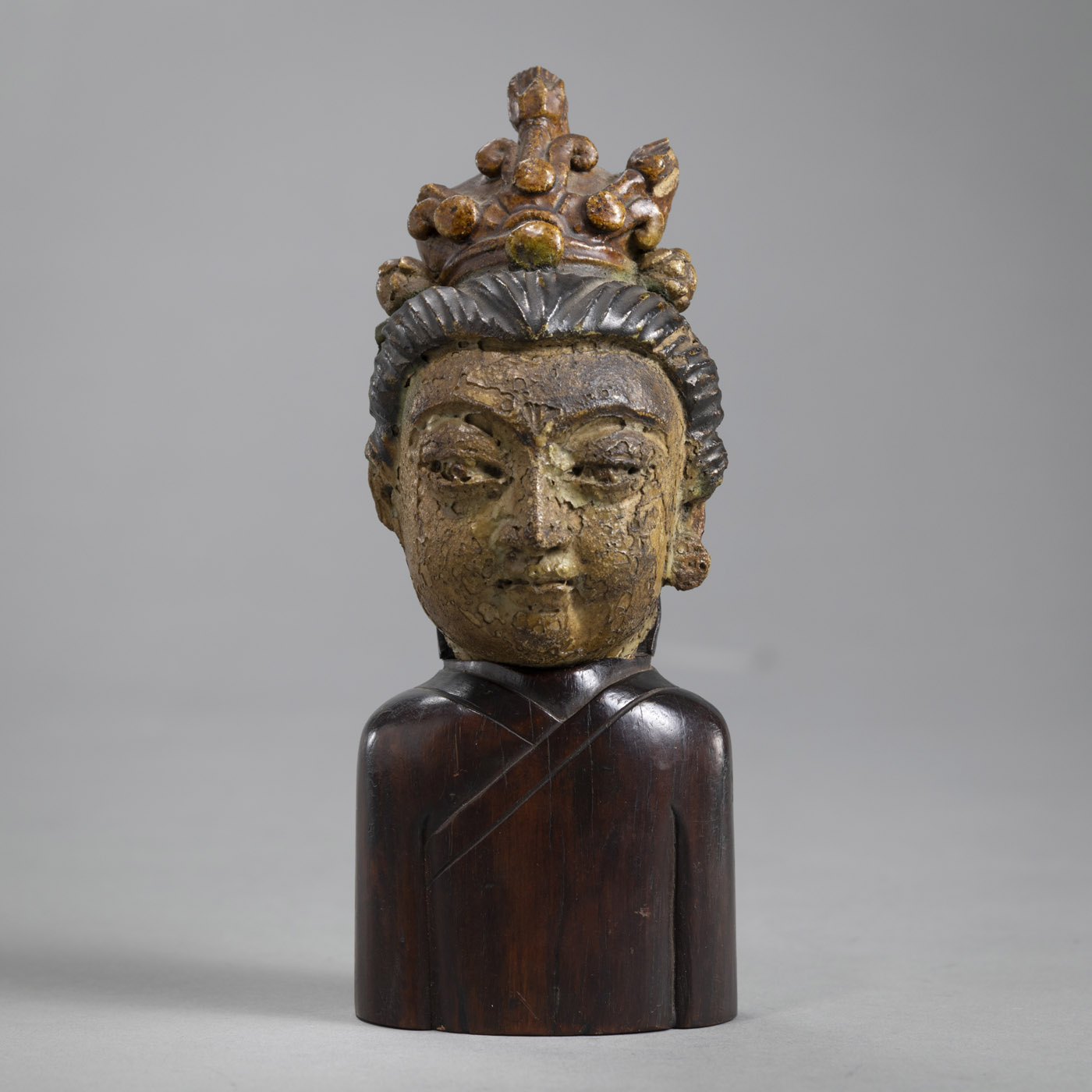A SMALL PARTLY PAINTED TERRACOTTA GUANYIN HEAD ON A WOOD STAND IN THE FORM OF A TORSO