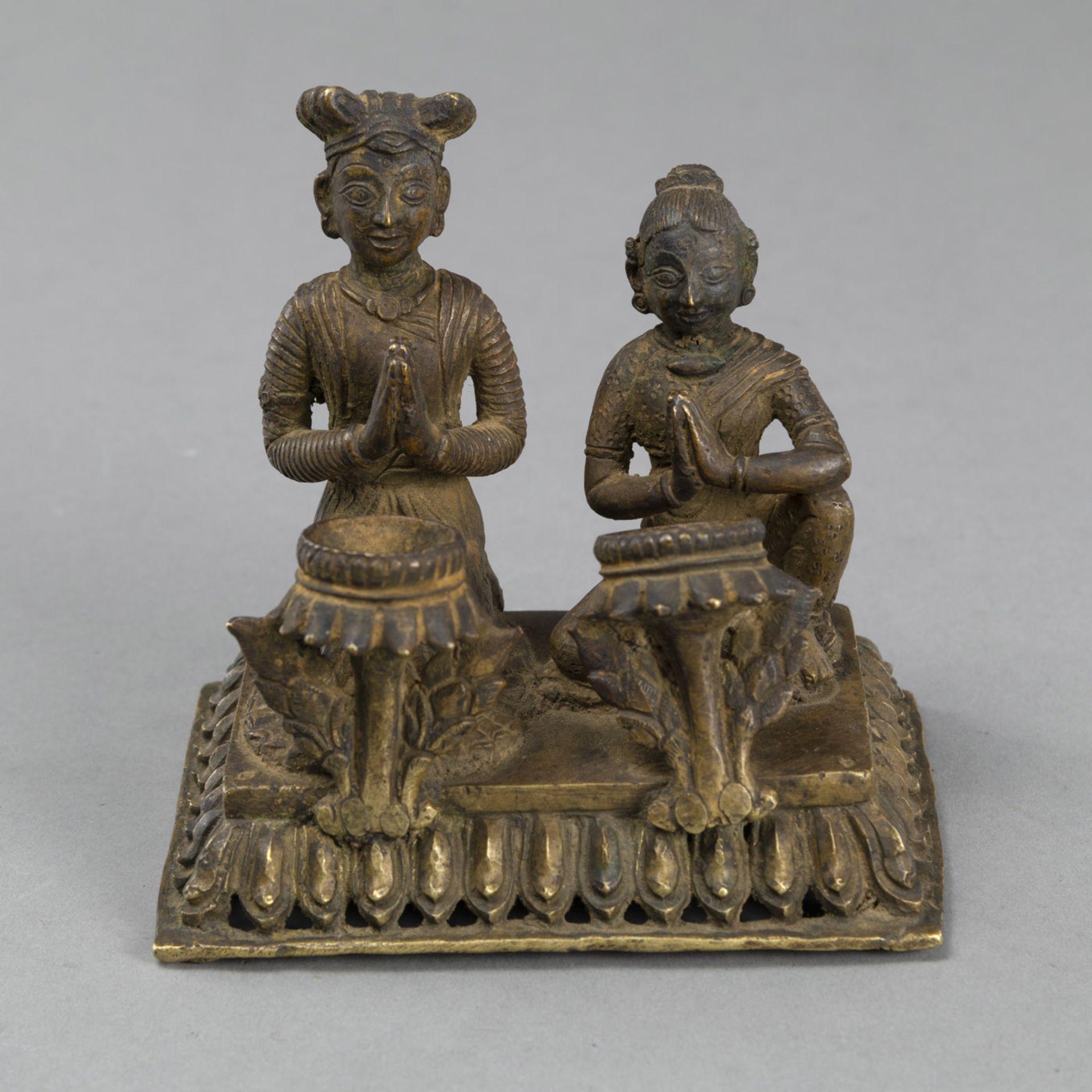 A GILT-COPPER OILLAMP WITH A KNEELING WORSHIPPING COUPLE ON A RECTANGULAR LOTUS BASE