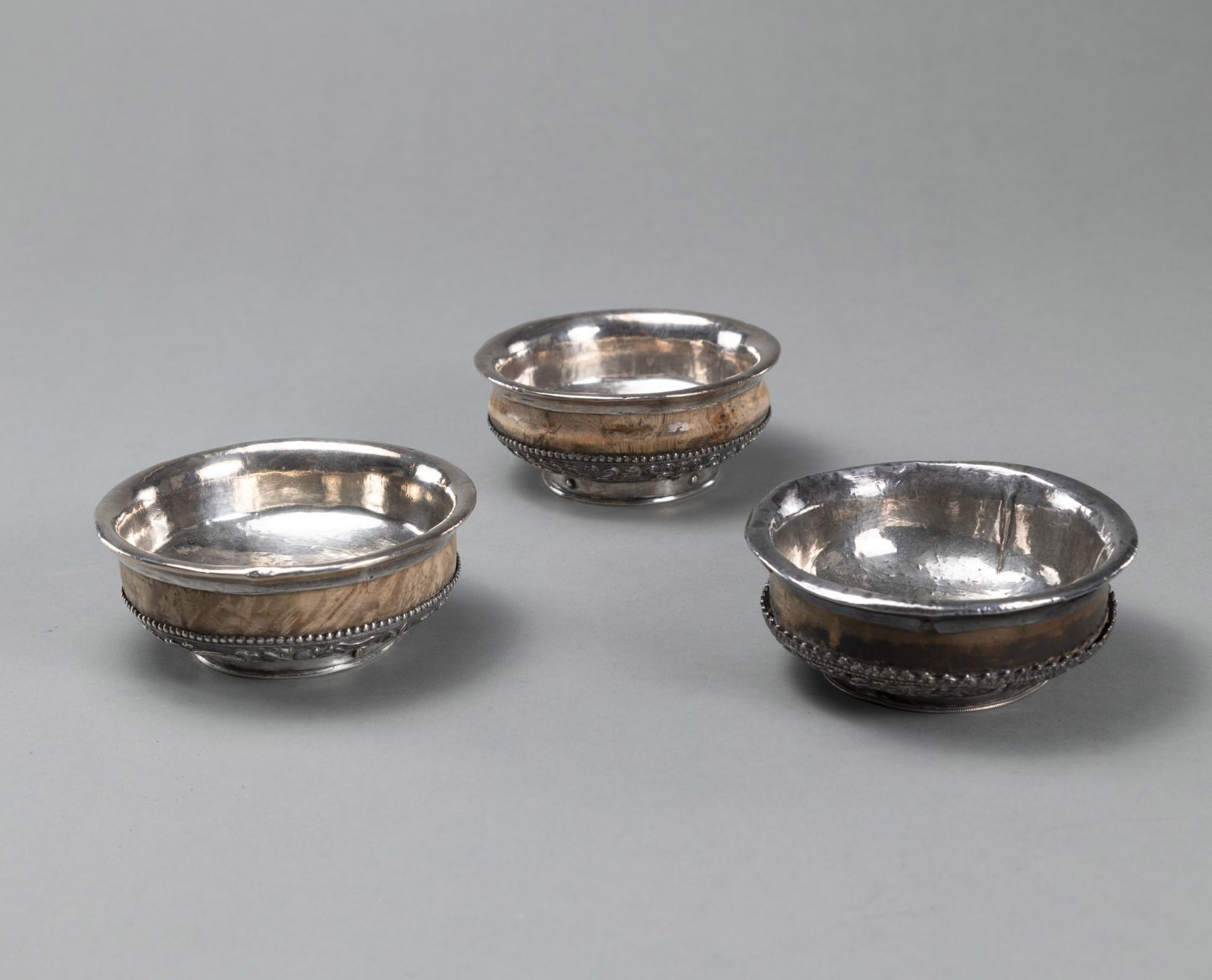 THREE ROOT WOODEN TEA BOWLS (PHORBA), PARTLY MOUNTED WITH SILVER, DECORATED WITH DRAGONS AND BUDDHI