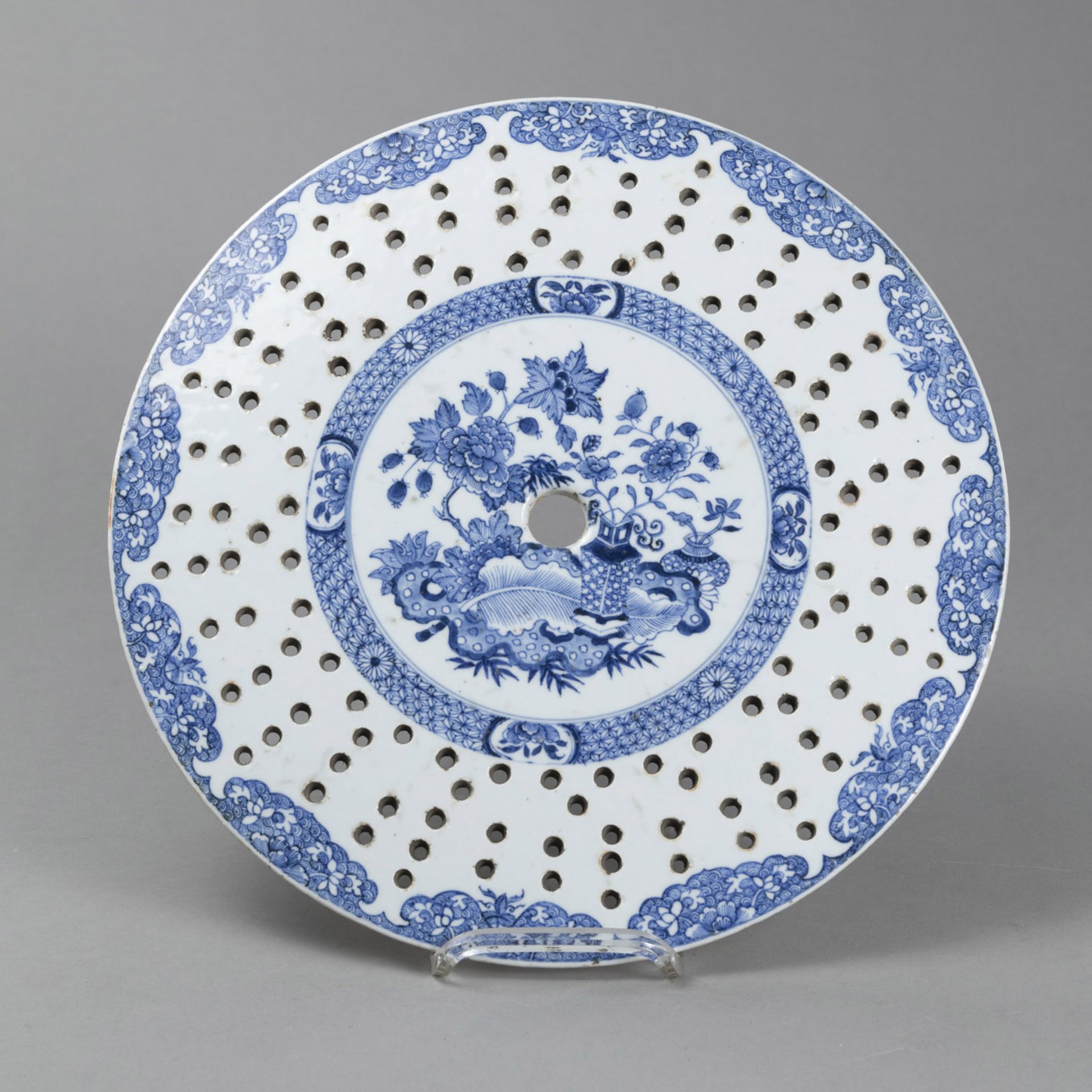 A CIRCULAR BLUE AND WHITE DRAINER WITH FLORAL DECORATION ON THREE SHORT FEET