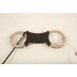 A set of stainless steel and black plastic Hiatt rigid handcuffs; 22cm long; (complete with key)