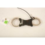 A set of stainless steel and black plastic Hiatt rigid handcuff, complete with key. (22cm long)