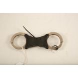 A set of stainless steel and black plastic Hiatt rigid handcuffs; 22cm long; (complete with key) RUC