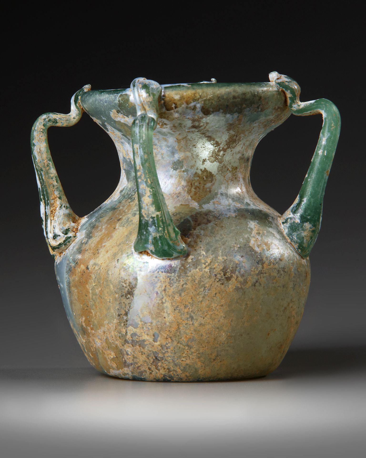 A ROMAN FOUR-HANDLED GREEN GLASS JAR, CIRCA 3RD CENTURY A.D.